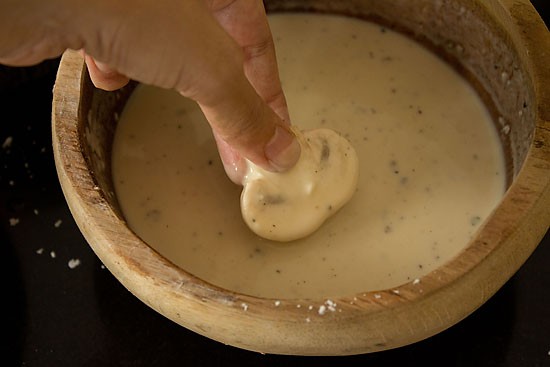 dipping mushroom in batter for mushroom manchurian recipe.