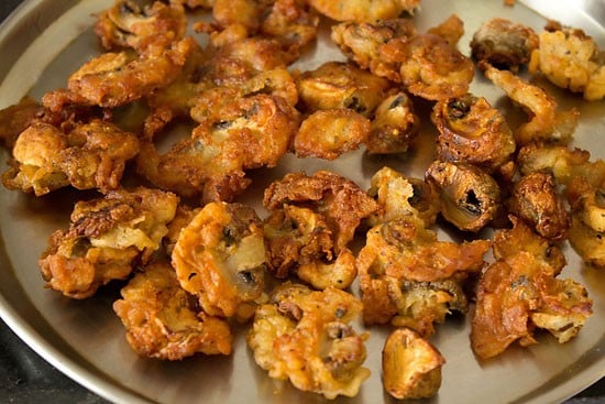 battered and fried mushrooms are golden brown, resting on a plate.