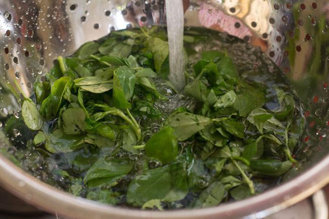 rinsing methi leaves under running water in a colander.