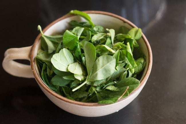 fresh methi leaves in a large mug.