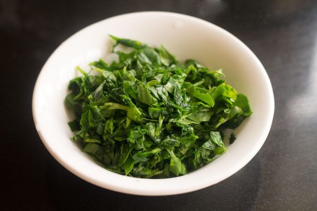 bright green chopped methi leaves in a small white prep bowl.