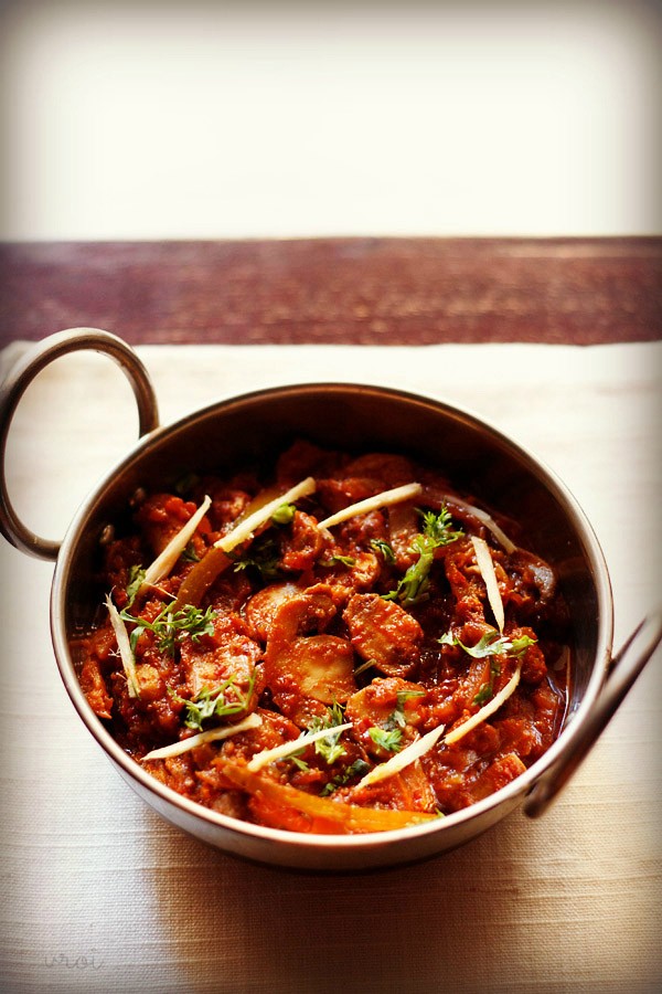 kadai mushroom garnished with coriander leaves, ginger julienne and served in a steel kadai on a white napkin on a dark ebony colored board