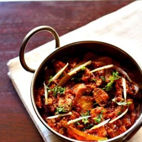 kadai mushroom garnished with coriander leaves, ginger julienne and served in a steel kadai on a white napkin on a dark ebony colored board