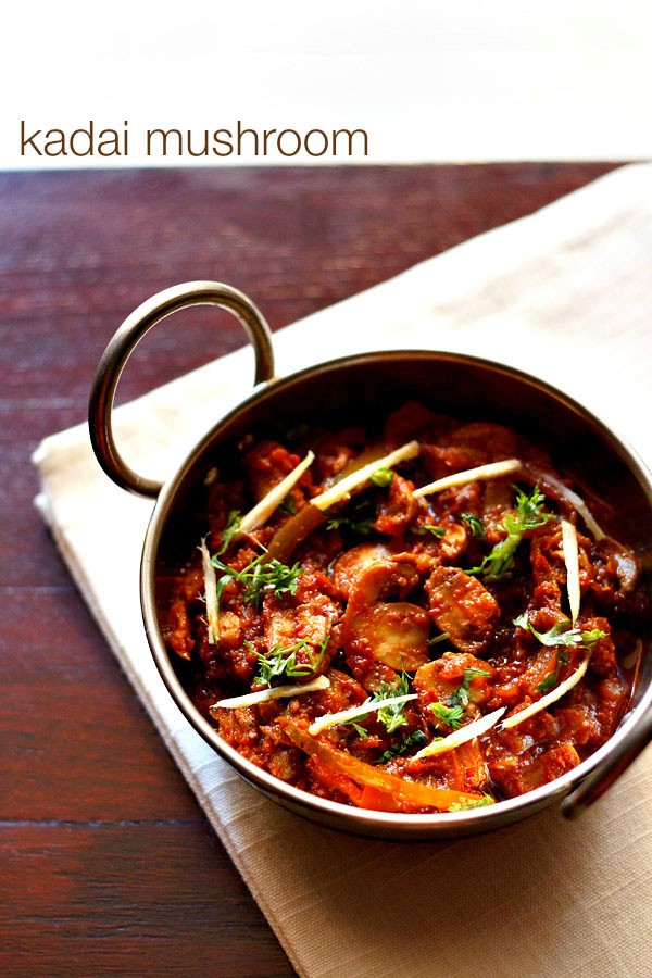 kadai mushroom garnished with coriander leaves, ginger julienne and served in a steel kadai on a white napkin on a dark ebony colored board