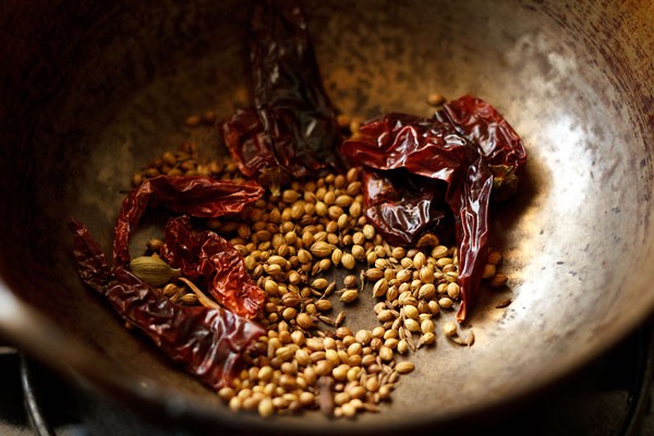 whole spices being roasted in a brass kadai (wok)