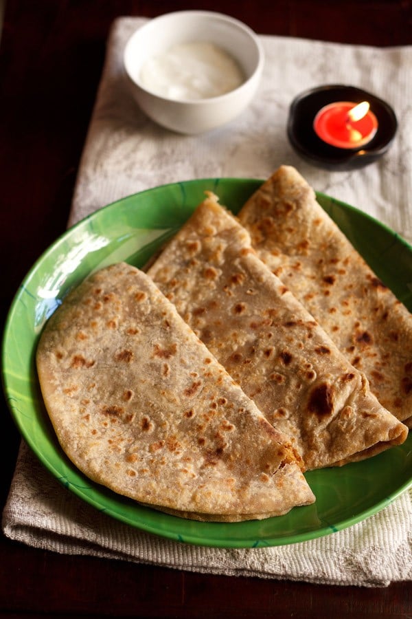 three puran poli on a green plate with a red tealight in the background