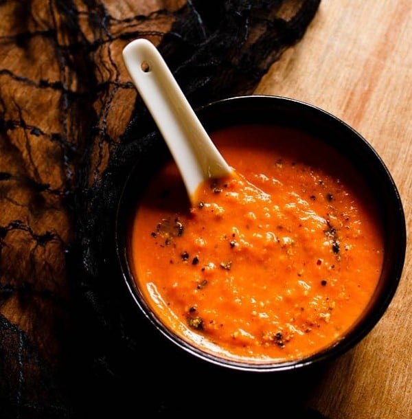 roasted tomato soup in a black bowl on a wooden table with a white soup spoon.