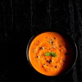 roasted tomato soup with a mint sprig in the center in a black bowl on a black fabric.