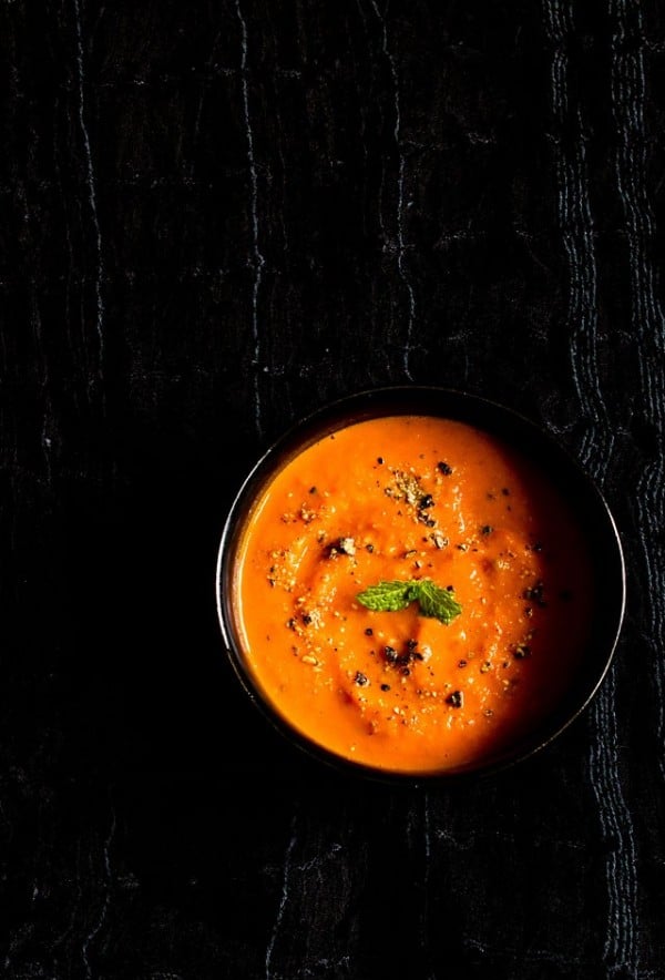 roasted tomato soup with a mint sprig in the center in a black bowl on a black fabric