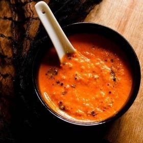 roasted tomato soup in a black bowl on a wooden table with a white soup spoon.