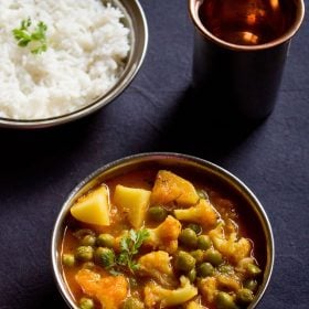 aloo gobi matar curry served in a steel bowl with a side of steamed rice in bowl and glass of water