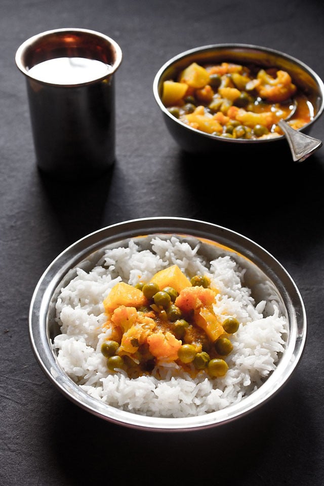 aloo gobi matar served on steamed rice in a steel bowl
