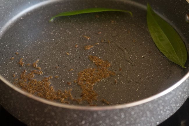 frying cumin seeds and bay leaf in hot oil in pan 