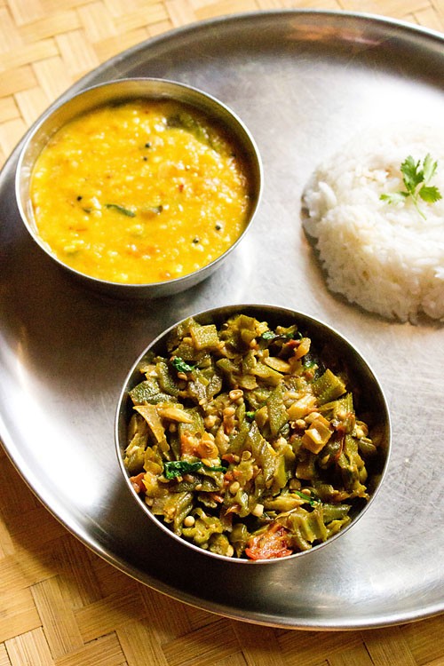 bhindi ki sabji served with dal and steamed rice in steel bowls.