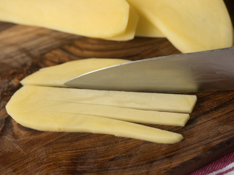 thin slices of potatoes being cut into french fry shapes