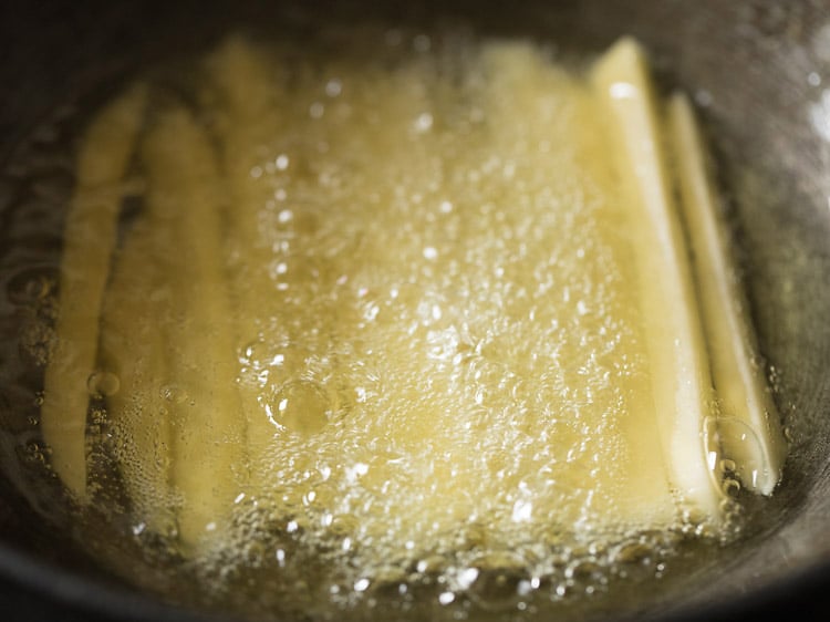 potato sticks frying in oil for first step of french fries recipe
