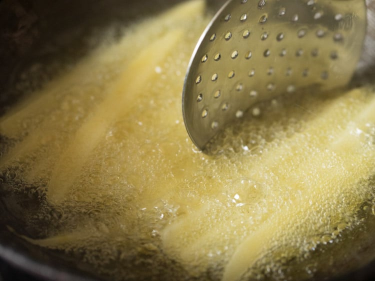 stirring french fries in oil with a slotted spoon