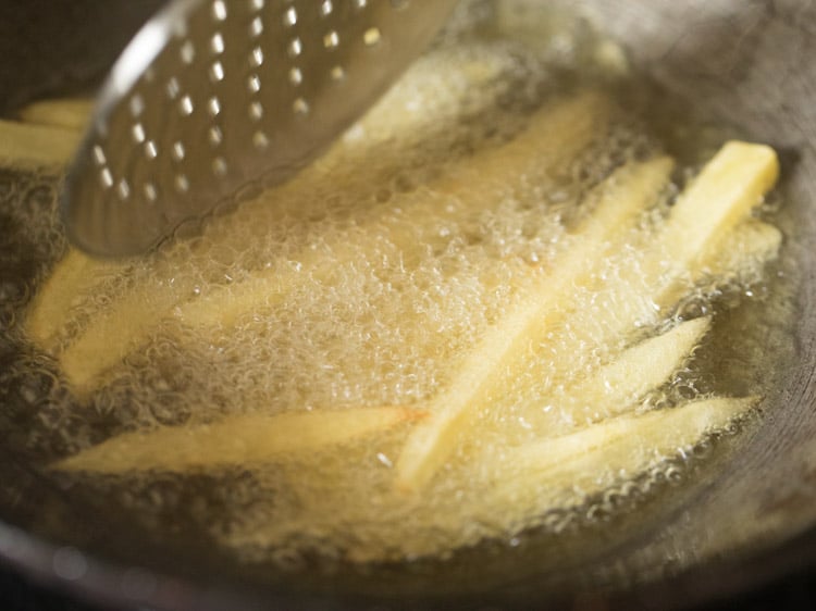 slotted spoon stirring french fries in oil