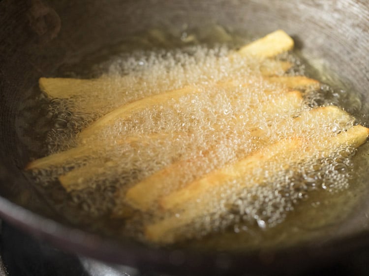 potatoes starting to turn golden in shimmering bubbling oil in a wok