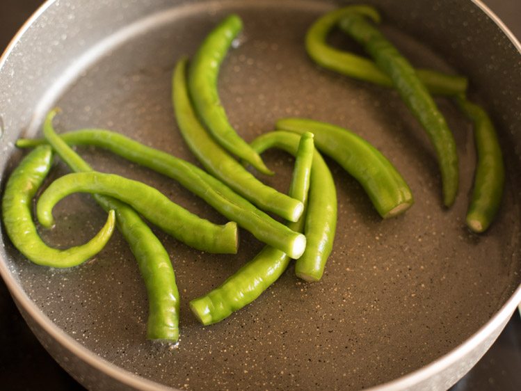 adding slit green chilies in hot oil in pan