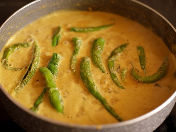 adding fried green chilies to masala curry mixture in pan