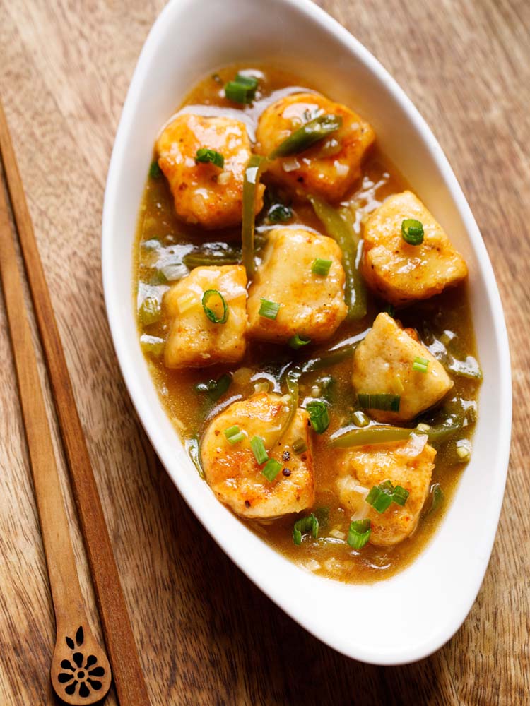 instant pot chilli paneer served in an oval white bowl with wooden chopsticks on left side on a wooden board