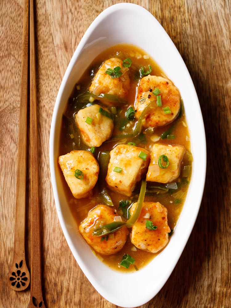 instant pot chilli paneer served in an oval white bowl with wooden chopsticks on left side on a wooden board