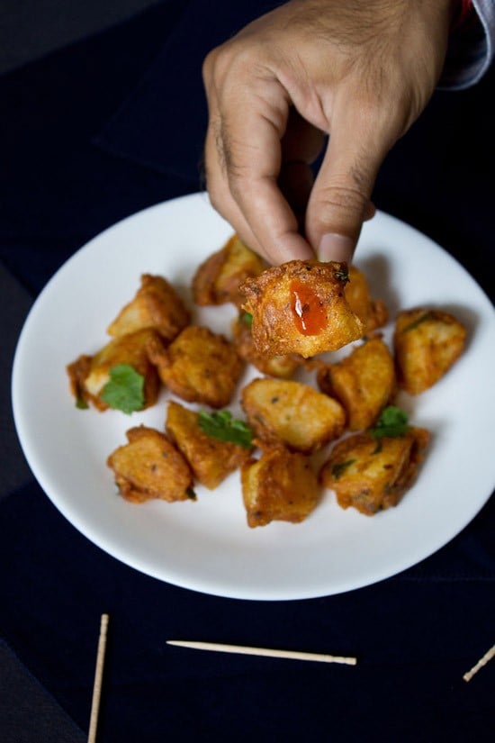 hand holding a piece of aloo 65 with some sauce on it. 