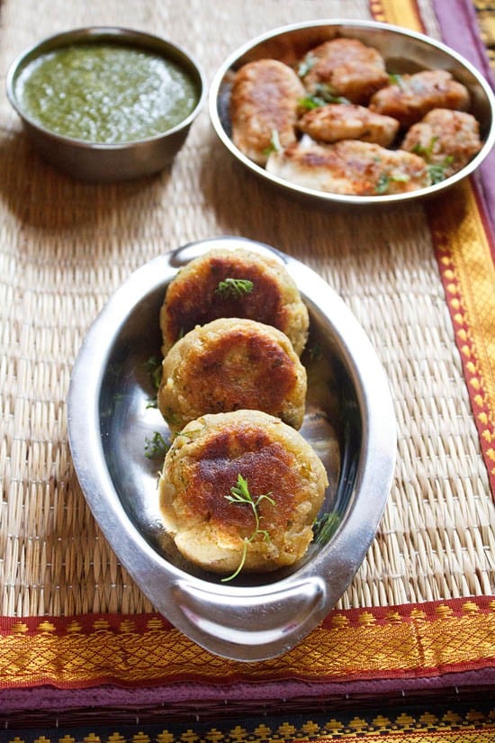 sweet potato cutlets garnished with coriander leaves and served in a steel platter with green chutney in a small steel bowl. 
