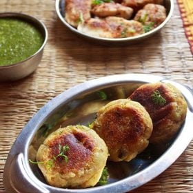 sweet potato cutlets garnished with coriander leaves and served in a steel platter with green chutney in a small steel bowl.