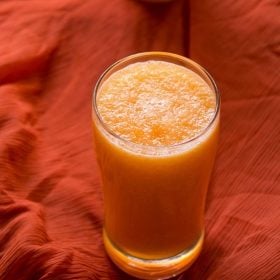 muskmelon juice or cantaloupe juice in two tall clear glasses on an orange piece of fabric.