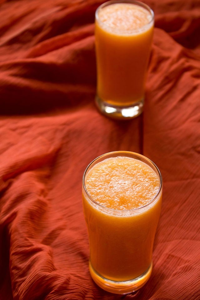 kharbooja juice or musk melon juice in two tall clear glasses on an orange piece of fabric.