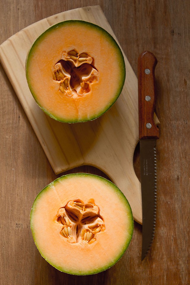 halved musk melon or cantaloupe on a wooden cutting board.