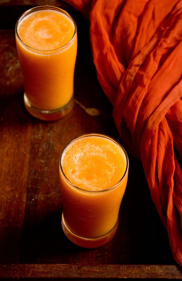 cantaloupe juice or muskmelon juice in two tall clear glasses on a wooden table next to an orange piece of fabric