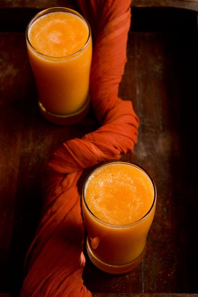 overhead shot of muskmelon juice recipe divided between two glasses on a wooden table.