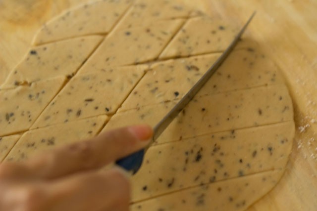 rolled dough being cut with a knife to make diamonds. 