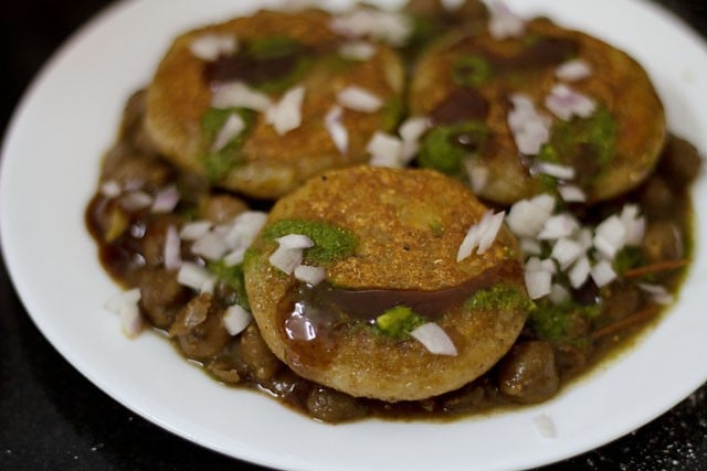 chutneys and chopped onions on top of tikkis on chole 