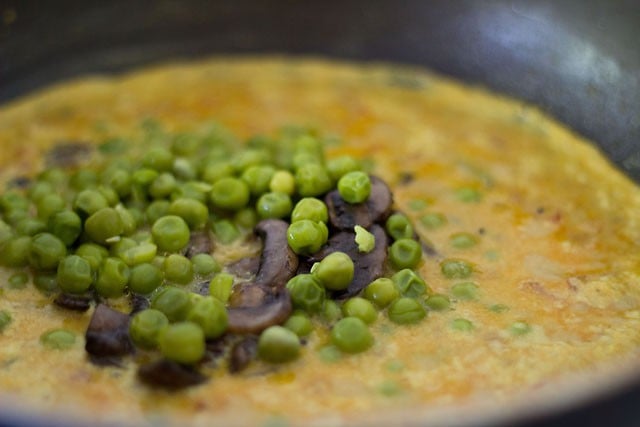 adding sautéed mushrooms and cooked green peas to curry 