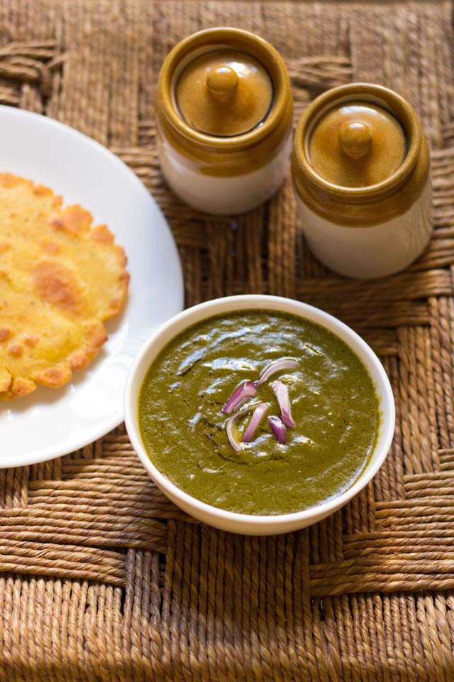 sarson ka saag in a white bowl topped with chopped onions and served with a piece of makki ki roti.