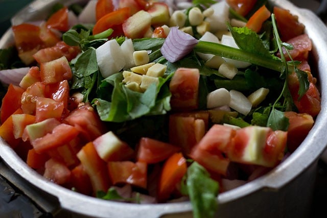 adding veggies to pressure cooker with the greens for making punjabi sarson ka saag recipe.