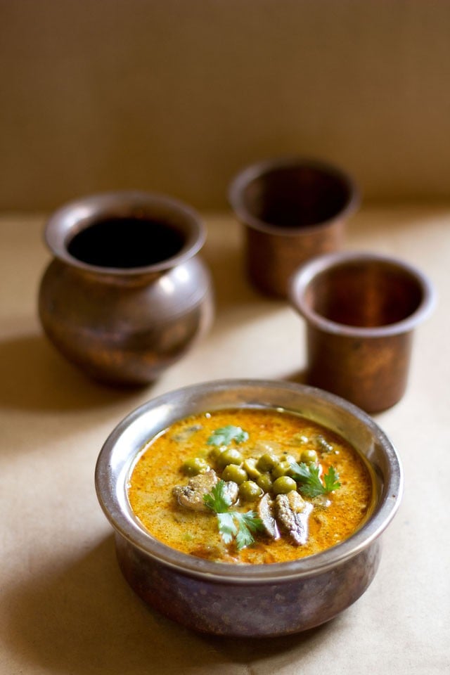 mushroom peas curry or batani curry served in a metallic small pan with copper glasses in the background