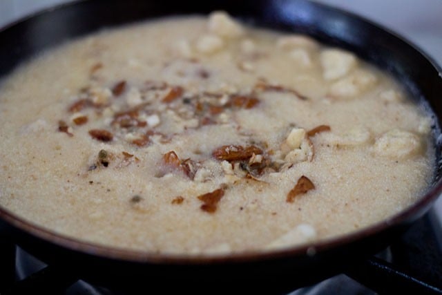 adding hot water or milk, green cardamom powder and dry fruits to semolina in pan.