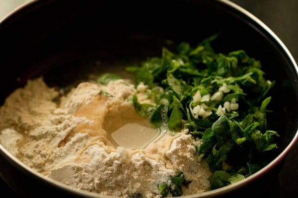 tepung gandum, garam, daun methi, cili hijau, bawang putih cincang, minyak dan air dalam mangkuk.