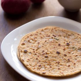 two onion paratha stacked in a square white plate with red onions and chopped onions, green chillies in a small white bowl in background