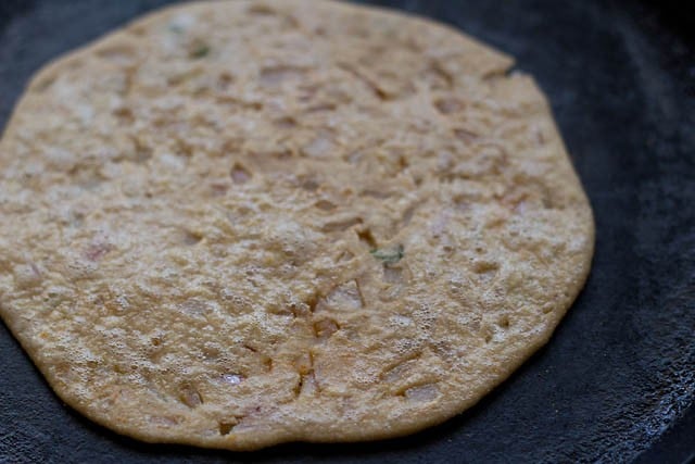 onion paratha roasting on a black skillet