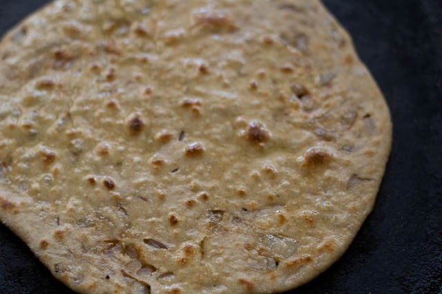onion paratha with some blisters and some oil spread on it on a black skillet