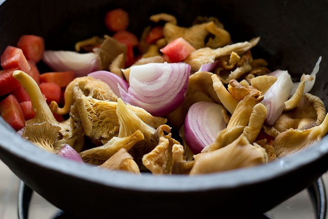 sliced onions, oyster mushrooms, carrots and veggies in a pot.