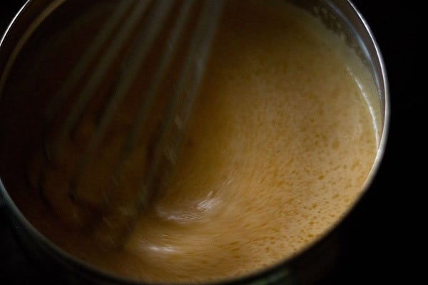 orange mixture with dissolved sugar being stirred with wired whisk