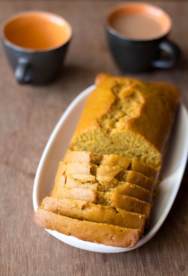 orange cake slices with the loaf on a white oblong tray on a wooden board.