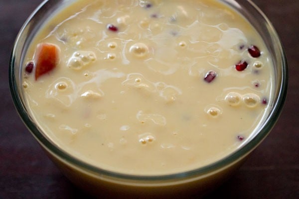 making fruit custard recipe, adding custard to fruits in bowl